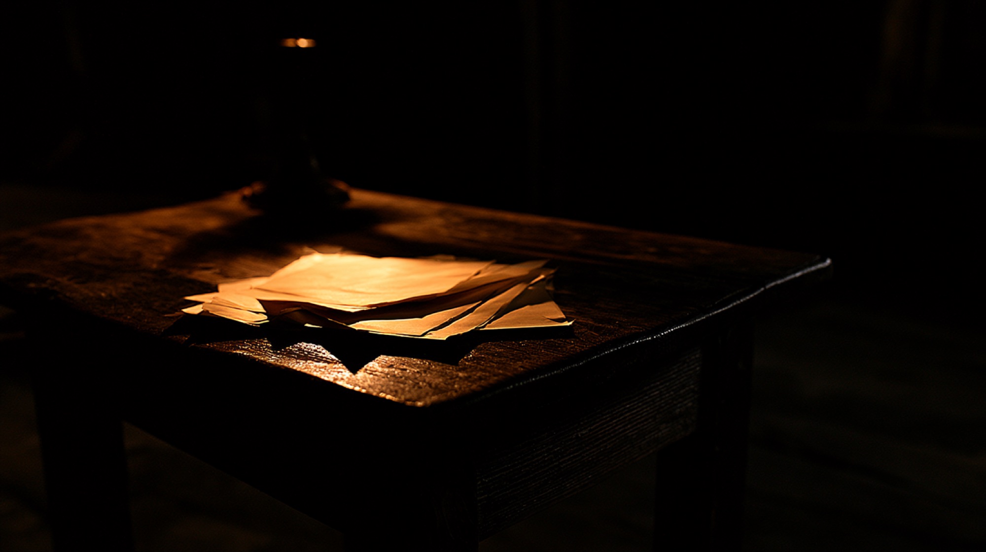 A few loose sheets of paper on a small wooden table, lit by a single lamp in a dark room.