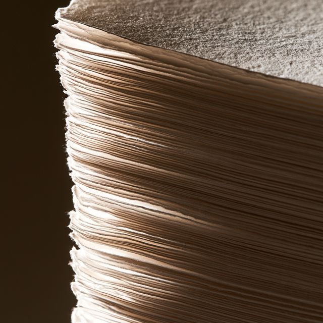 The cut edge of a thick stack of paper in low warm light.