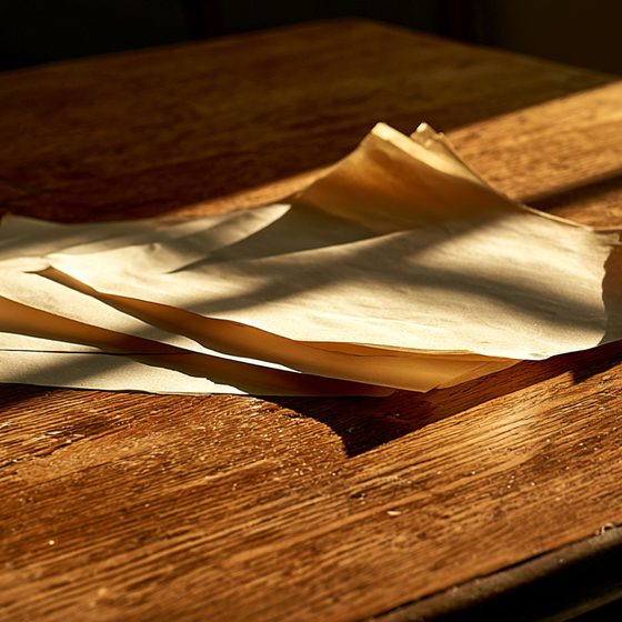 Low morning sun across a few loose pages on a bare wooden desk.